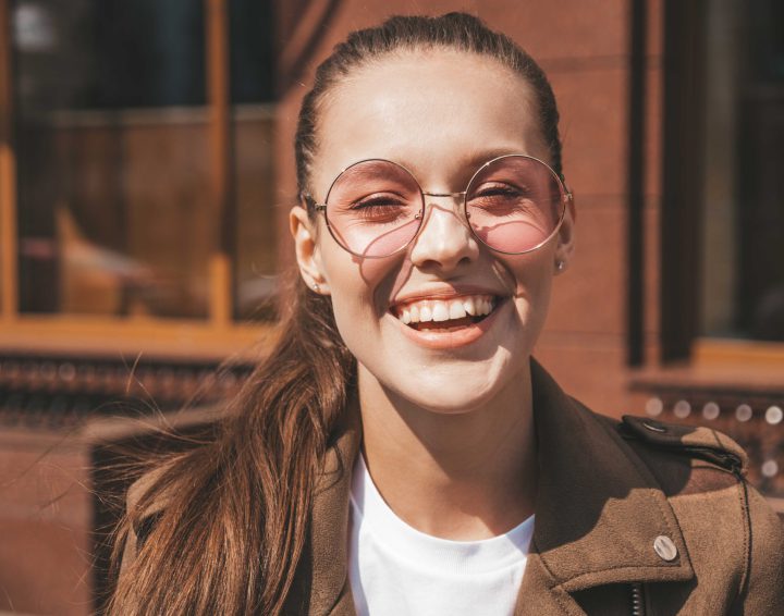 Portrait of beautiful smiling brunette model dressed in summer hipster jacket clothes. Trendy girl posing in the street background. Funny and positive woman in round sunglasses